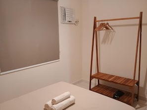 Ein schlichter Raum mit einer Holzhängeregalkombination, einem weißen Bett und einer Wandklimaanlage.