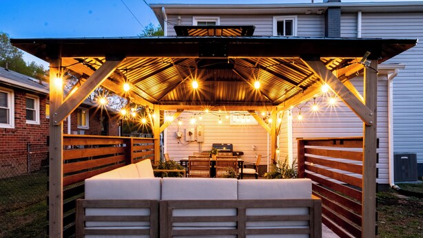 A covered outdoor seating area with a wooden bench and table, string lights, and a pergola structure.
