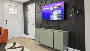 A modern living room with a flat-screen TV mounted on a dark wall, a light-colored sofa, and a green cabinet.