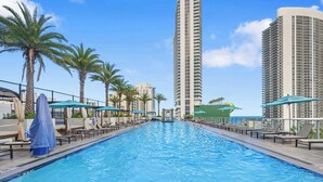 A swimming pool with lounge chairs and umbrellas, surrounded by tall buildings. - Luxury 32nd Floor Condo | Full Beach Club Access (Hollywood)