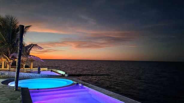 En swimmingpool med udsigt til solnedgang, palmer og en træterrasse.