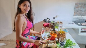 En person tilbereder mad ved et udendørs bord, med en grill i baggrunden.