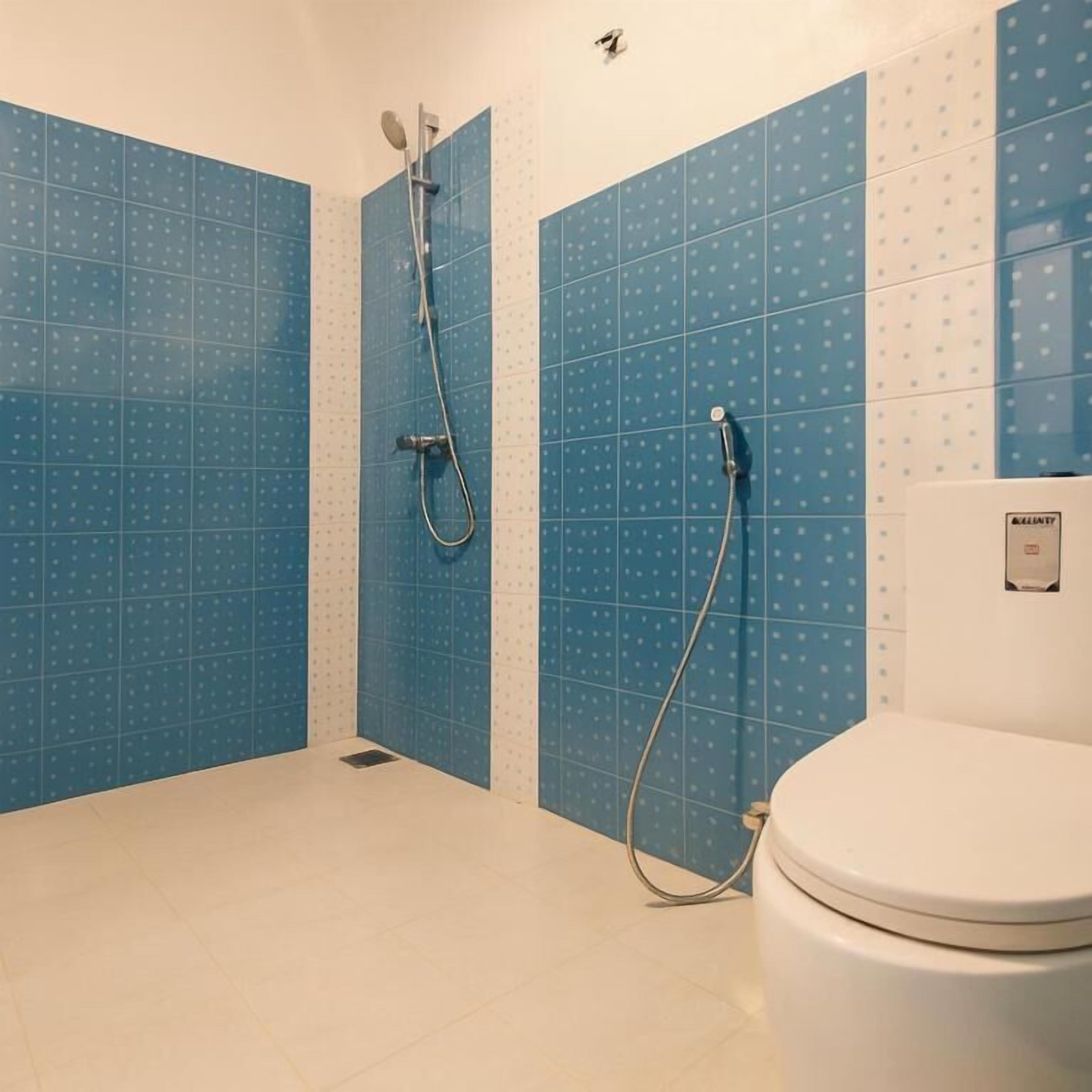 A bathroom with blue tiled walls, a white toilet, and a shower area.