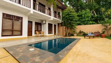 Una piscina al aire libre, sombrillas, sillones reclinables de piscina