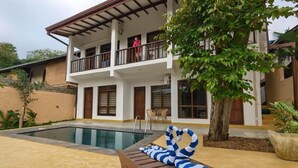 A two-story building with a balcony, a swimming pool, and a lounge area with a striped towel. - Bentota Luxe Ayurveda (Bentota)