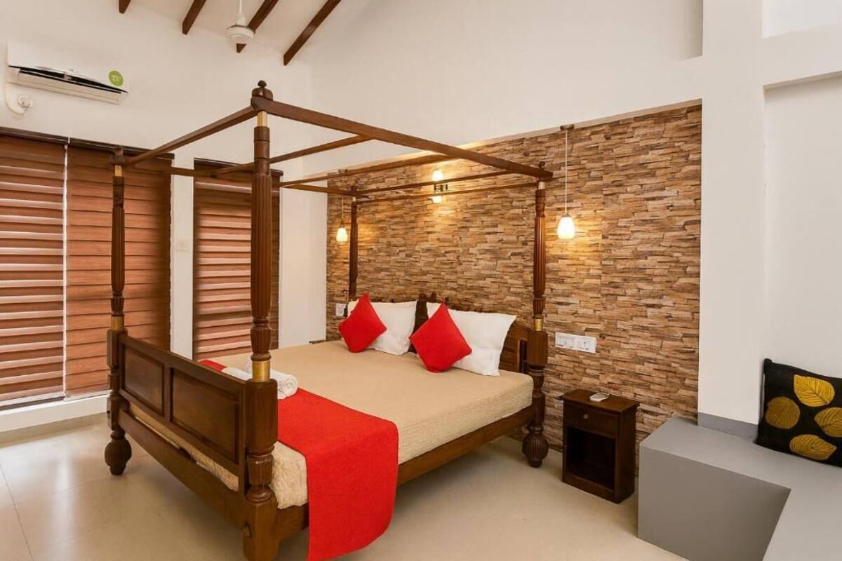 Un letto a baldacchino con struttura in legno e dettagli rossi, una parete in pietra con illuminazione a incasso e un comodino con una lampada.