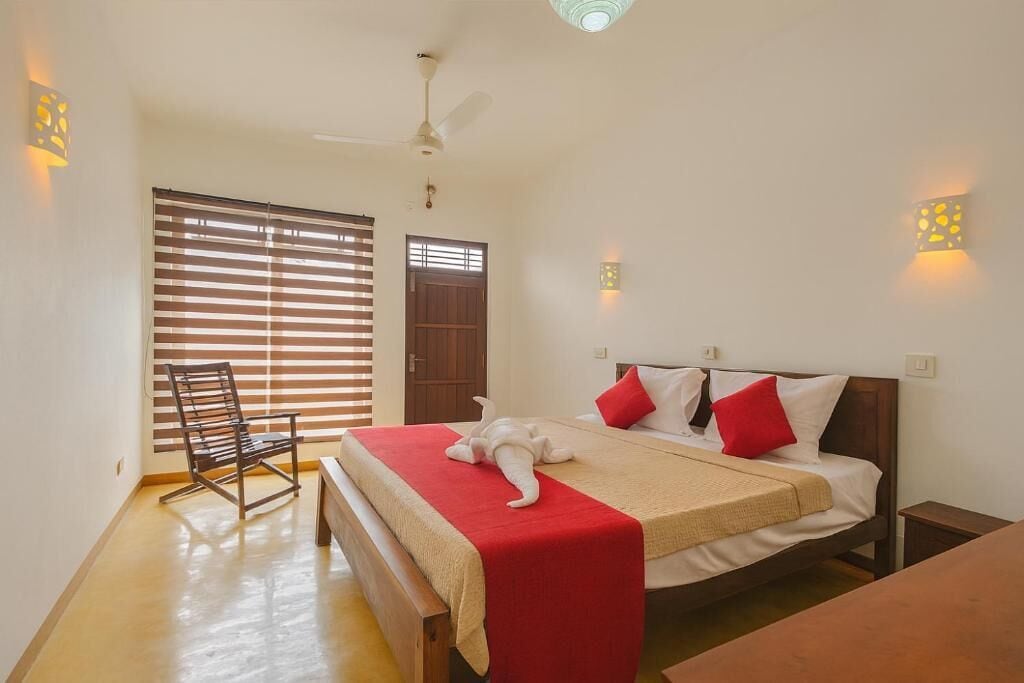 Une chambre à coucher comprenant un lit, une chaise, un ventilateur de plafond et une fenêtre avec des stores.