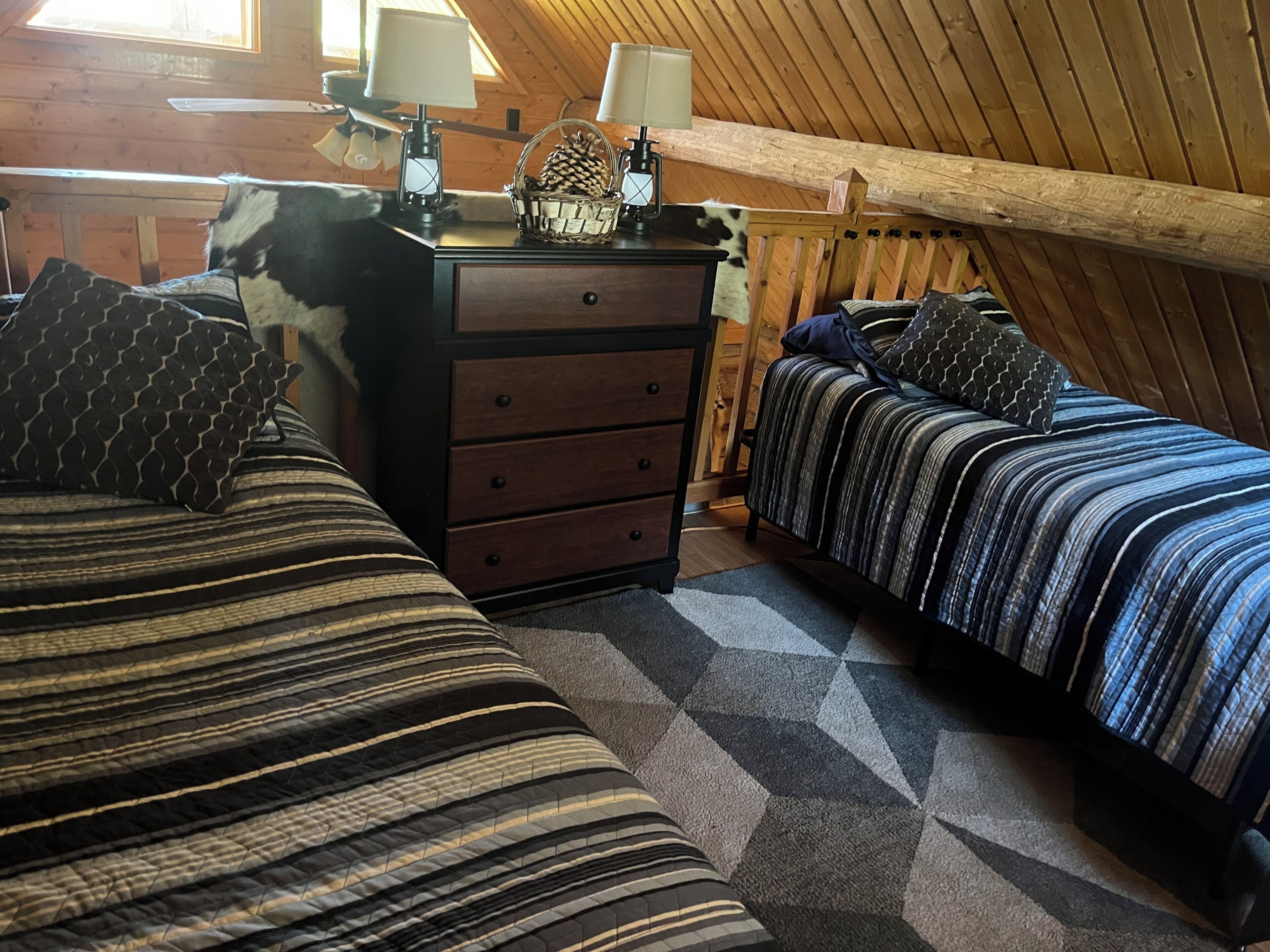 Une chambre mansardée chaleureuse, avec deux lits, une commode et une lampe.