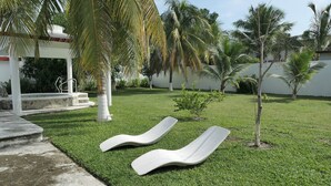 Un giardino curato con piscina, palme e due poltrone bianche.