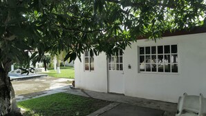 Un edificio bianco con una porta e finestre, circondato dal verde e un vialetto in cemento.