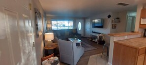 Ein Wohnzimmer mit Sofa, Couchtisch, Fernseher und einer Küchenzeile mit Arbeitsplatte und Schränken.