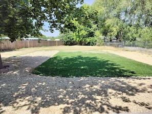 A backyard with a green lawn, gravel area, and a wooden fence.