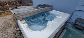 A hot tub with a cover, surrounded by a wooden fence and a blue building.