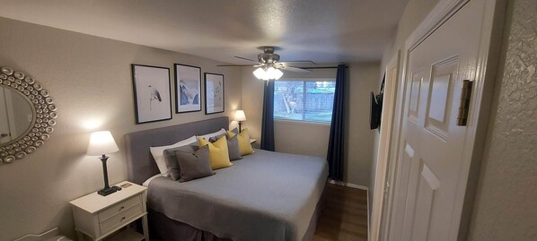 Ein Schlafzimmer mit einem Bett, einem Nachttisch mit Lampe, einem Deckenventilator und gerahmten Bildern an der Wand.