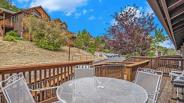 A wooden deck with a round table and chairs, overlooking a hillside with cabins. - Sprague Mountain Condo #6247 (Estes Park)