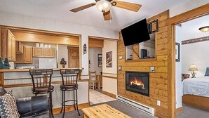 A cozy room with a fireplace, wooden walls, a ceiling fan, and a television mounted on the wall. - Sprague Mountain Condo #6247 (Estes Park)