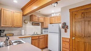 A kitchen with wooden cabinets, a refrigerator, a microwave, and a stove. - Sprague Mountain Condo #6247 (Estes Park)