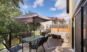 Une terrasse extérieure avec une table et des chaises, un grand parasol et une vue sur une maison en arrière-plan.