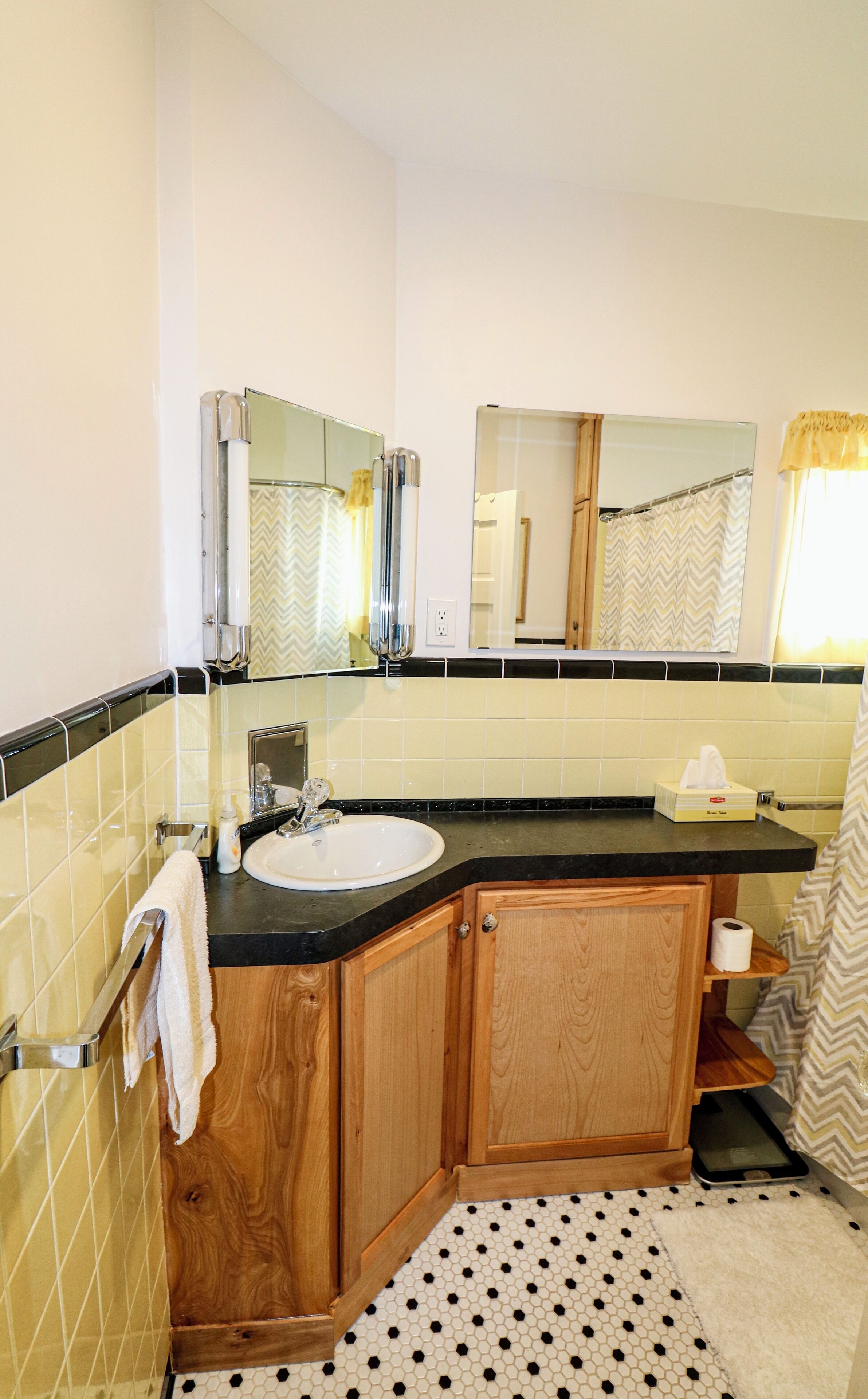 Un baño con lavamanos blanco, armarios de madera, un espejo y piso estampado.