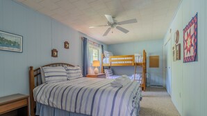 Quarto com uma cama de solteiro, uma cama beliche, uma mesa de cabeceira, um abajur e um ventilador de teto.