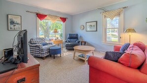Uma sala de estar com um sofá xadrez, um sofá vermelho, uma mesa de centro de madeira, uma poltrona azul e uma televisão sobre um armário de madeira.