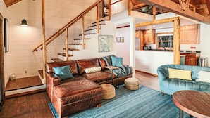 Ein großzügiger Wohnbereich mit einer Holztreppe, Ledersofas und einer Küche im Hintergrund.
