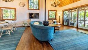 Ein geräumiges Wohnzimmer mit einer großen, blauen Couch, Holzboden und großen Fenstern mit Blick ins Freie.