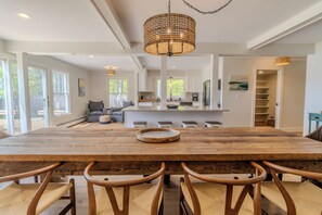 Un vaste espace dédié à la salle à manger, avec une grande table en bois et six chaises, un îlot central doté d’appareils de cuisine, et une vue sur l’extérieur grâce à de grandes fenêtres.