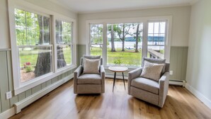 Ein Zimmer mit zwei Sesseln, die zu einem großen Fenster mit Blick auf einen Garten und einen See blicken.