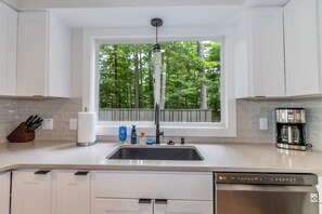 A modern kitchen with white cabinetry, a stainless steel dishwasher, and a coffee maker. - Gather and Relax on Little Glen Lake at Blue Haven (Empire)