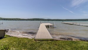 Ein Betonsteg, der in einen See führt, mit grasbewachsenen Ufern und Hügeln im Hintergrund.