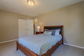 A bedroom with a bed, a nightstand, a lamp, and a door. - Lovely Views of Lake Leelanau at Bluebird Landing (Cedar)