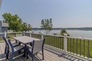 A deck with a table and chairs, overlooking a lake with a distant shoreline. - Lovely Views of Lake Leelanau at Bluebird Landing (Cedar)