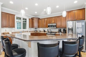 A kitchen with wooden cabinets, stainless steel appliances, and a large island with bar stools. - Spacious Private home for 14 at Blue Valley (Traverse City)