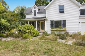 A two-story house with a porch, a stone foundation, and a garden with various plants and flowers. - Ideal Suttons Bay Retreat at Broadway Base Camp (Suttons Bay)