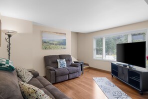 A living room with a sofa, a recliner, a television, and a painting on the wall. - Ideal Suttons Bay Retreat at Broadway Base Camp (Suttons Bay)