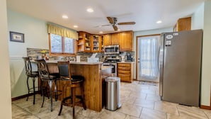 A kitchen with wooden cabinets, a stainless steel refrigerator, a microwave, a coffee maker, and a ceiling fan. - Ideal Suttons Bay Retreat at Broadway Base Camp (Suttons Bay)
