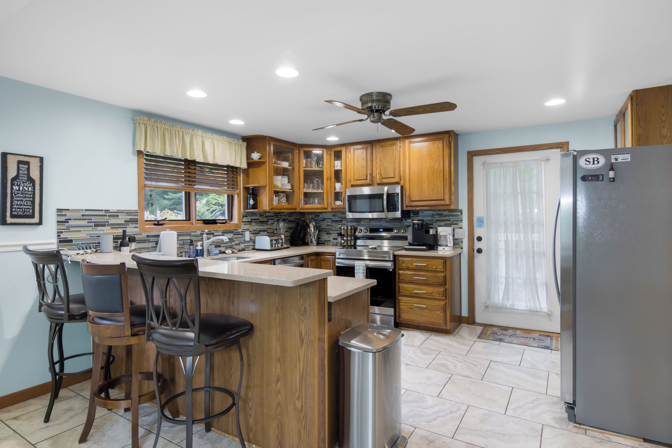 A modern kitchen with wooden cabinets, a stainless steel refrigerator, and a bar area with stools.