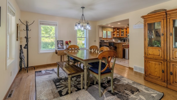 A dining area with a wooden table, chairs, and a chandelier. There is a coat rack and a rug on the floor. - Ideal Suttons Bay Retreat at Broadway Base Camp (Suttons Bay)