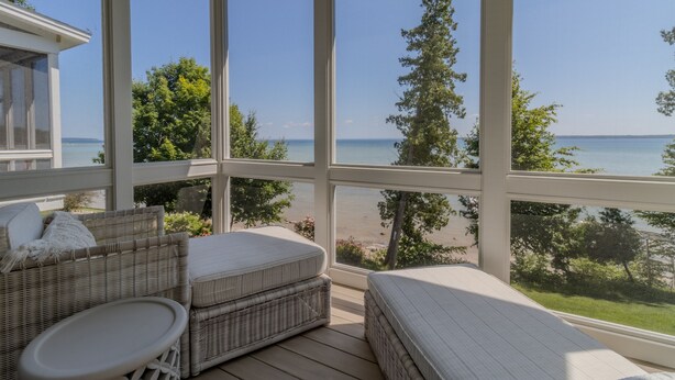 A sunlit room with wicker furniture, large windows, and a view of the beach and ocean.