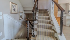A staircase with a wooden handrail and striped carpeted steps. - Dreamy Northern Michigan Escape, Chateau Sunrise (Suttons Bay)