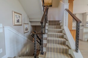 A staircase with a wooden handrail and striped carpeted steps. - Dreamy Northern Michigan Escape, Chateau Sunrise (Suttons Bay)