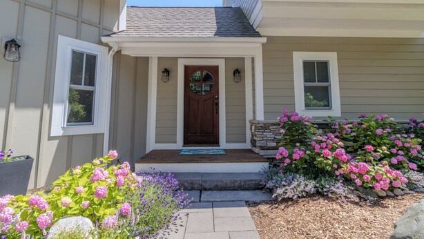 A house with a front porch, a wooden door, and a stone accent wall. - Dreamy Northern Michigan Escape, Chateau Sunrise (Suttons Bay)