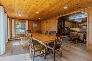 Ein Esszimmer mit Holztisch und -stühlen, ein Küchenbereich mit Holzschränken und ein Fenster mit Vorhängen.