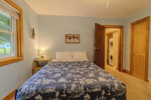 Un dormitorio con cama, mesita de noche, lámpara de pared, un cuadro colgado y una puerta que da a un cuarto de lavado.