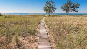 Ein Holzweg führt zu einem Strand mit zwei Bäumen und einer Bank.