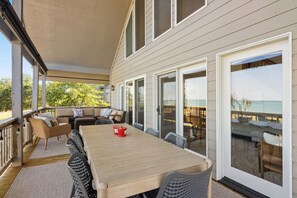Eine überdachte Terrasse im Freien mit einem Holztisch und -stühlen, einer Couch und Blick auf den Ozean.