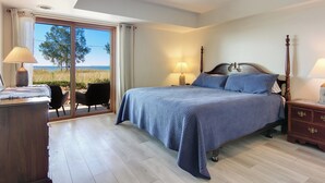 Ein Schlafzimmer mit einem großen Bett, zwei Nachttischen mit Lampen, einer Holzkommode und einer Glastür, die zu einem Außenbereich führt.