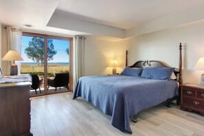 Ein Schlafzimmer mit einem großen Bett, zwei Nachttischen mit Lampen, einer Holzkommode und einer Glastür, die zu einem Außenbereich führt.