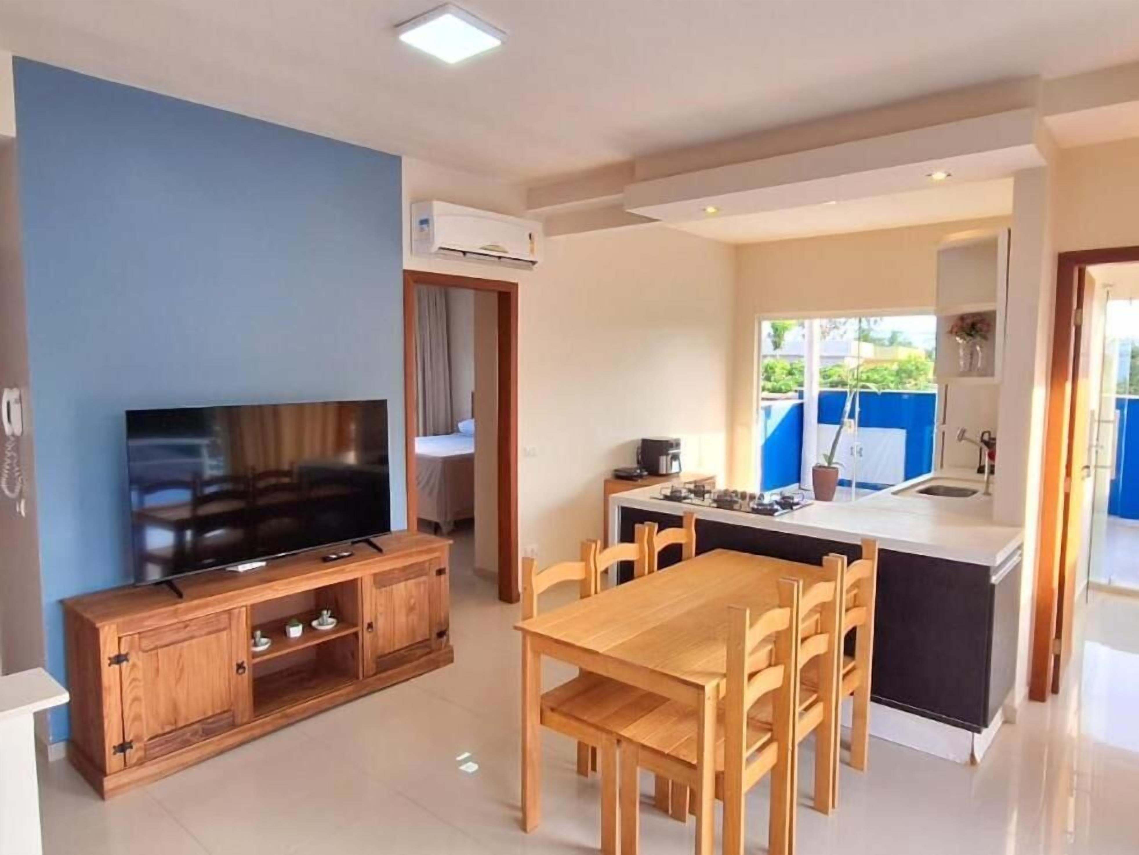 Una sala moderna con un televisor de pantalla plana, muebles de madera y una zona de cocina con una mesa de comedor y sillas.